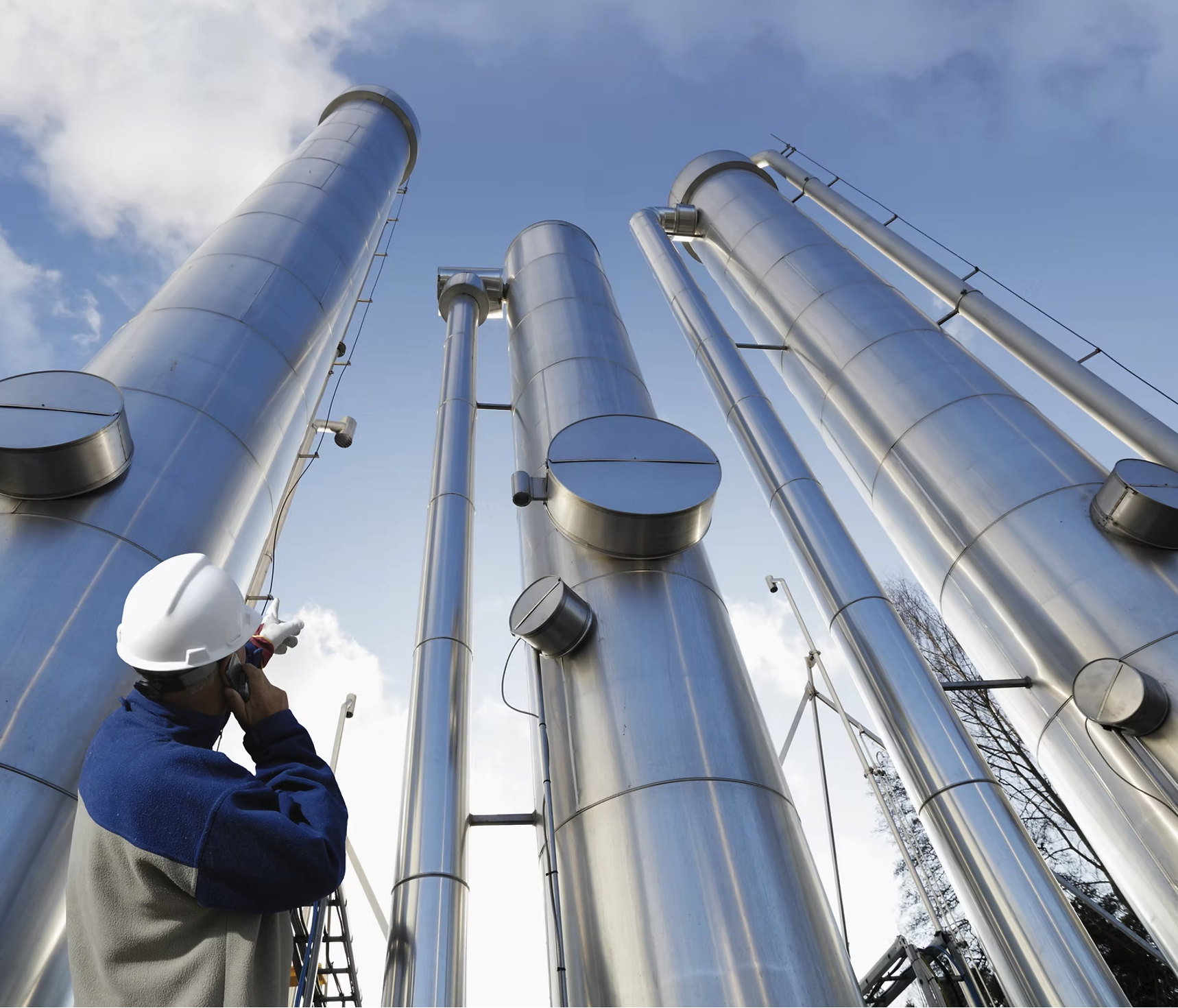 Un ingeniero con casco observa columnas de proceso de acero inoxidable